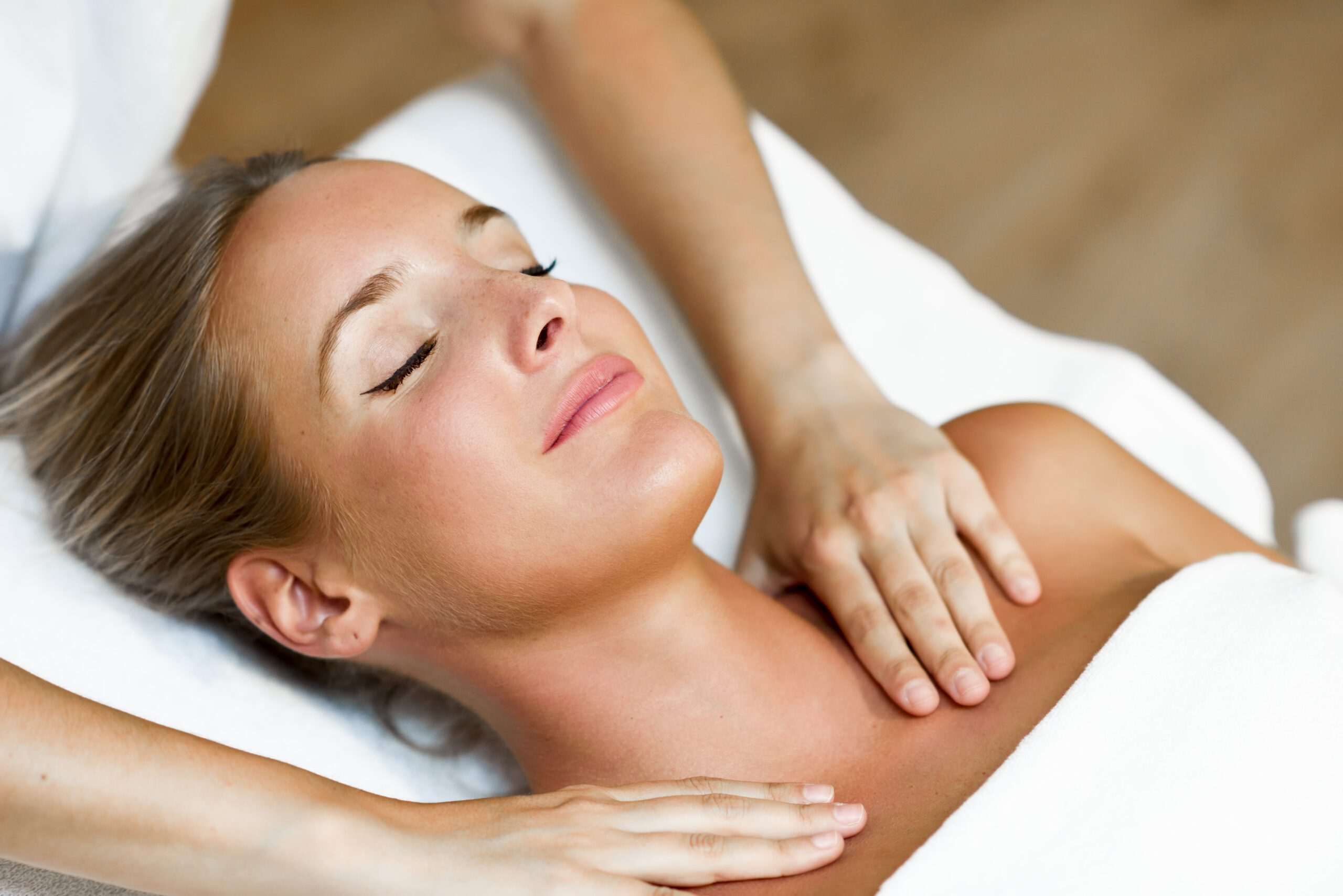 Young blond woman receiving a head massage in a spa center with eyes closed and smiling. Female patient is receiving treatment by professional therapist.